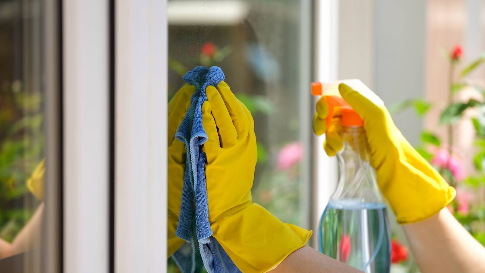 A close-up of someone cleaning windows with a spray bottle and microfibre cloth.